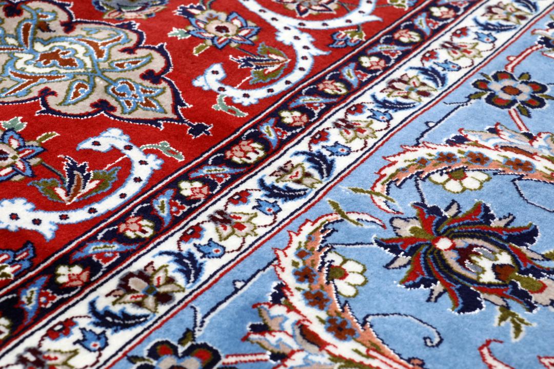Een vierkant handgeknoopt Isfahan-tapijt uit het Midden-Oosten met een rood centraal medaillon en blauwe randen.