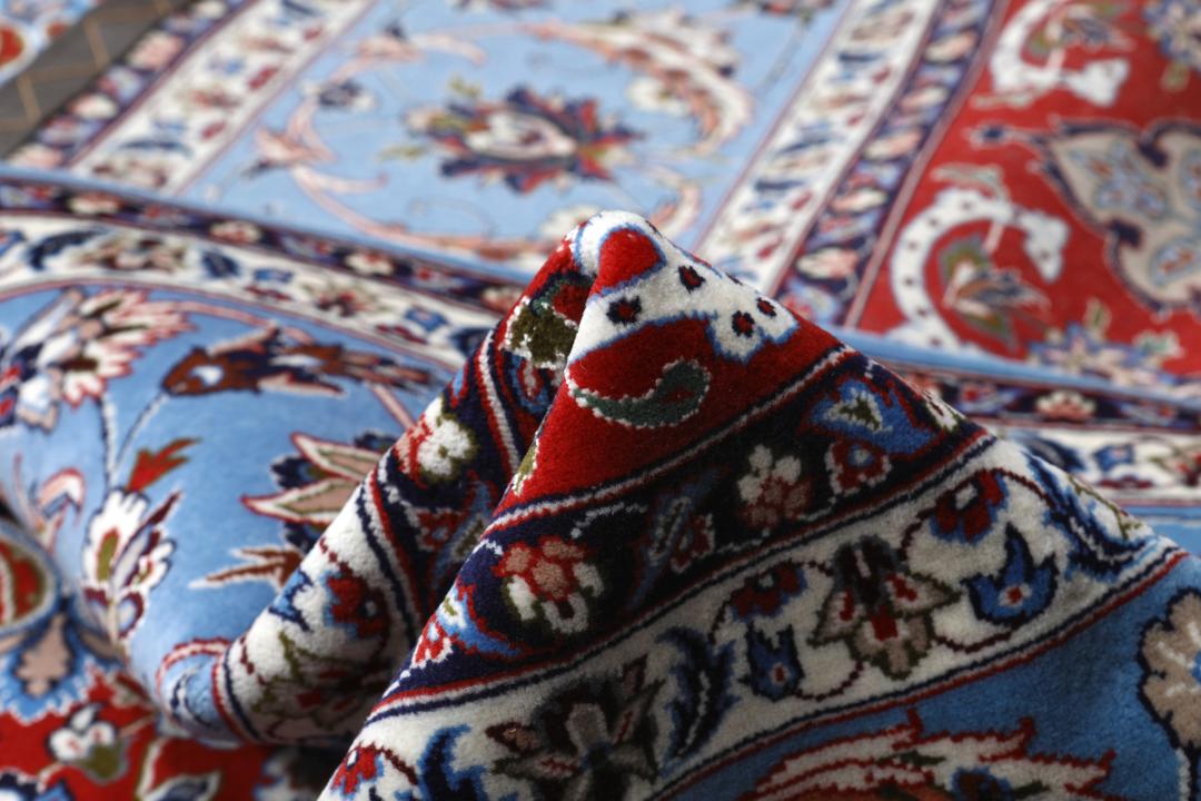 Een vierkant handgeknoopt Isfahan-tapijt uit het Midden-Oosten met een rood centraal medaillon en blauwe randen.