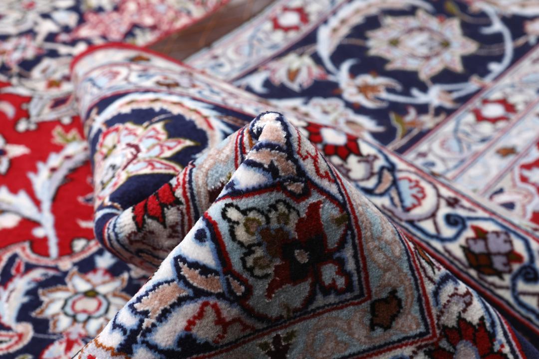 Et rødt og mørkeblåt Isfahan-tæppe fra Mellemøsten med dekorative blomstermønstre.