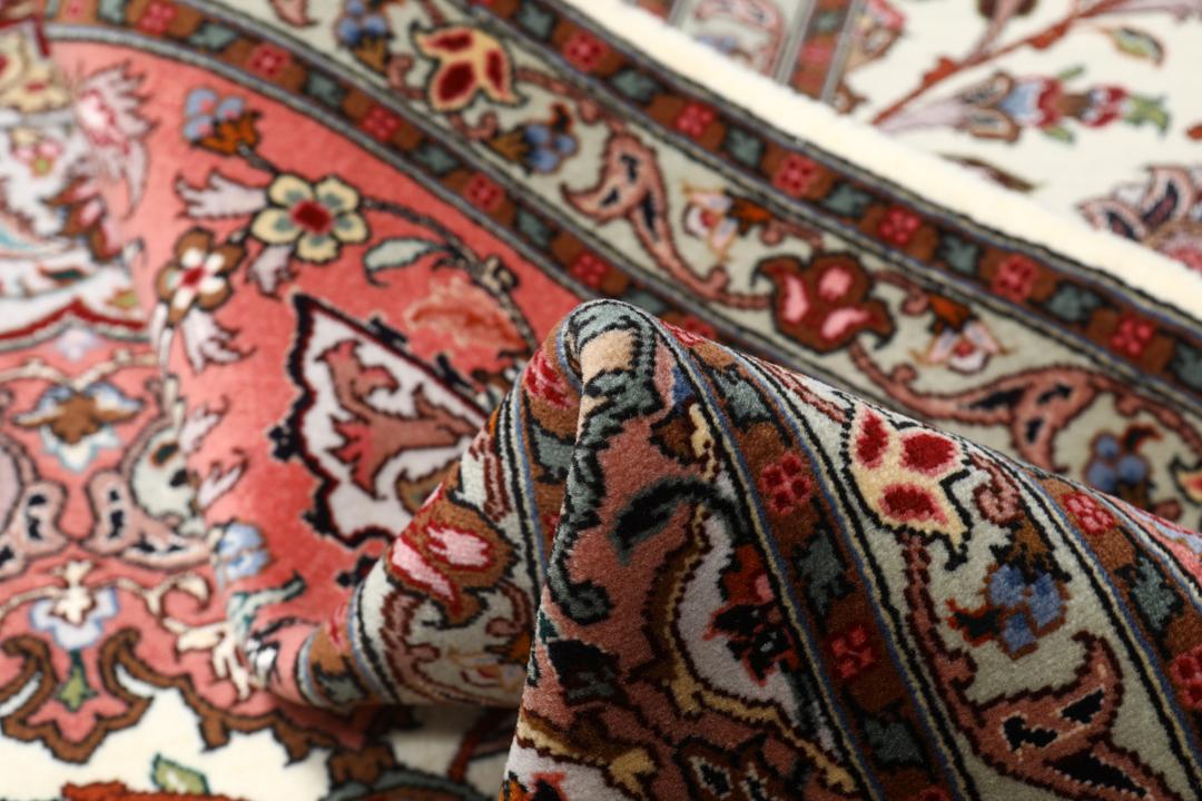 Et rødt og beige håndknyttet Tabriz-tæppe med en central medaljon og blomstermotiver.