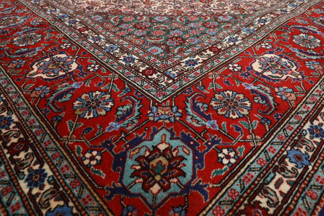 Et stort rektangulært Tabriz-tæppe med en central medaljon og dekorative blomstermønstre i rød, blå og creme.