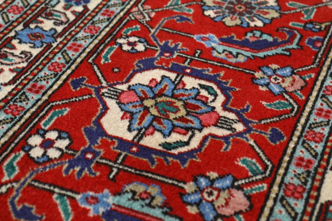 Et stort rektangulært Tabriz-tæppe med en central medaljon og dekorative blomstermønstre i rød, blå og creme.
