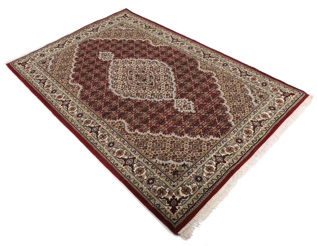 Een handgeknoopt Tabriz-tapijt uit India met een centraal medaillon op een rode ondergrond.