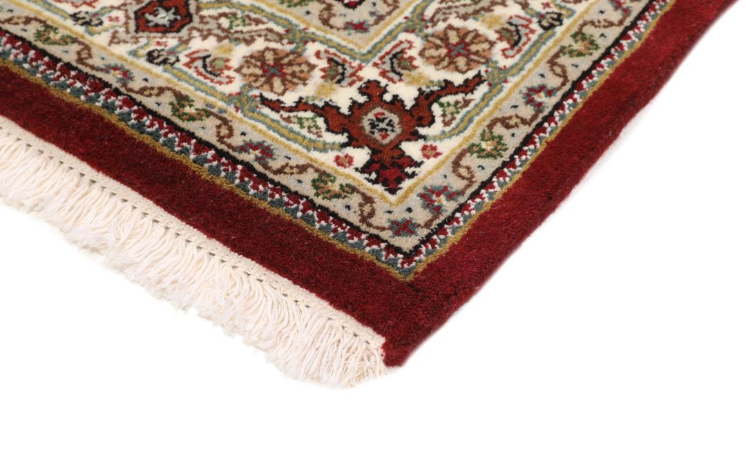 Een handgeknoopt Tabriz-tapijt uit India met een centraal medaillon op een rode ondergrond.