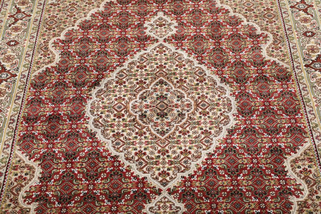 Een handgeknoopt Tabriz-tapijt uit India met een centraal medaillon op een rode ondergrond.