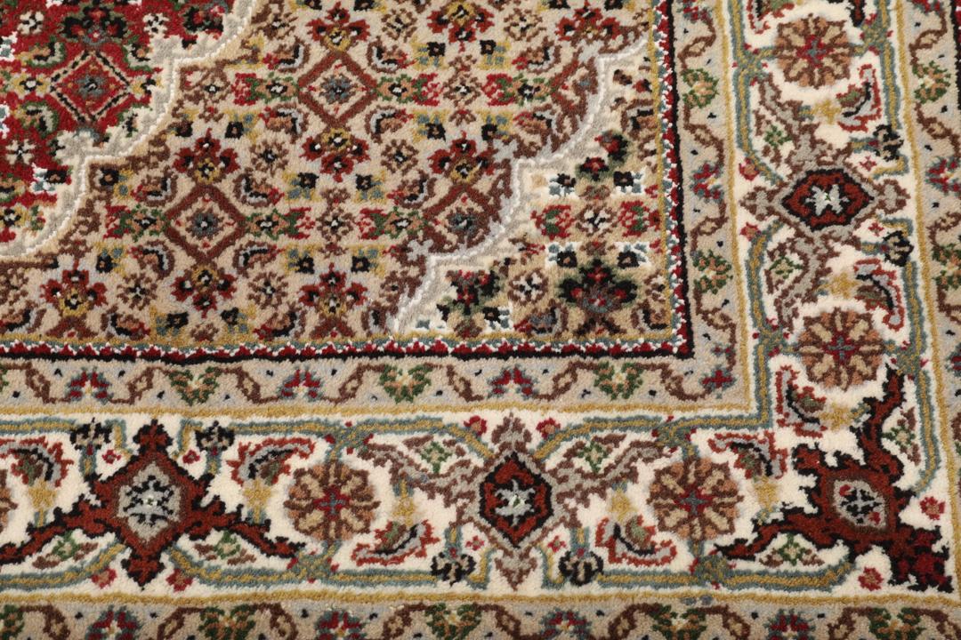 Een handgeknoopt Tabriz-tapijt uit India met een centraal medaillon op een rode ondergrond.