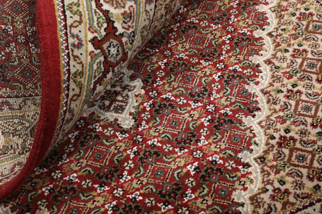 Een handgeknoopt Tabriz-tapijt uit India met een centraal medaillon op een rode ondergrond.