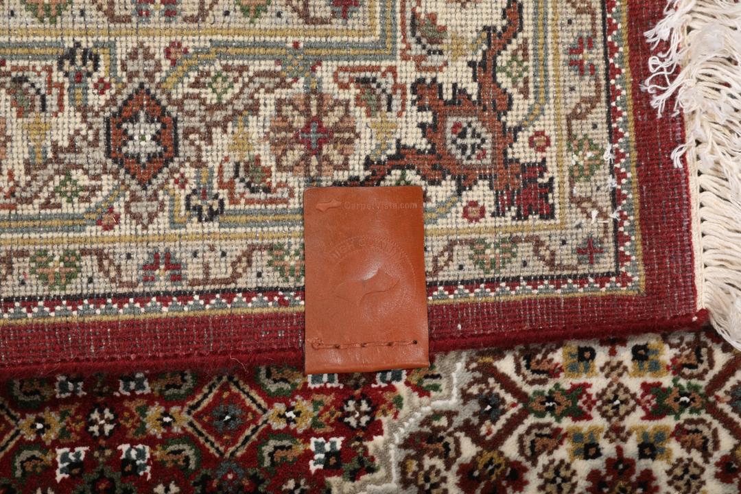Een handgeknoopt Tabriz-tapijt uit India met een centraal medaillon op een rode ondergrond.