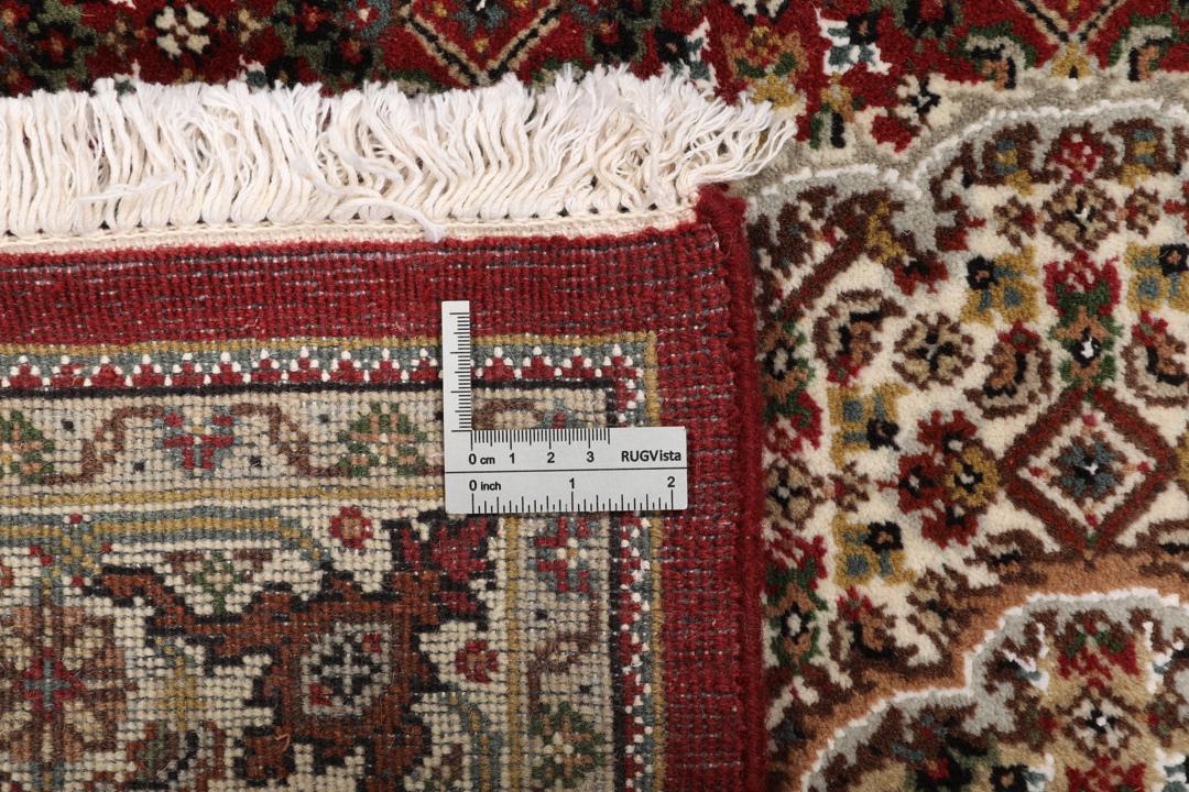 Een handgeknoopt Tabriz-tapijt uit India met een centraal medaillon op een rode ondergrond.