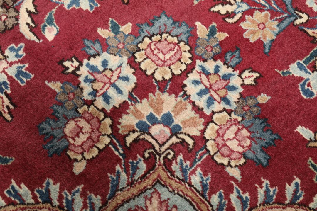 Hand-knotted Mashad rug from the Middle East featuring a dark-red field with intricate floral patterns.