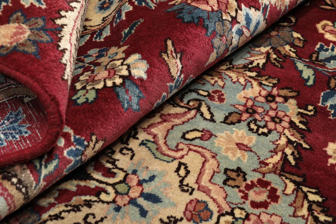 Hand-knotted Mashad rug from the Middle East featuring a dark-red field with intricate floral patterns.