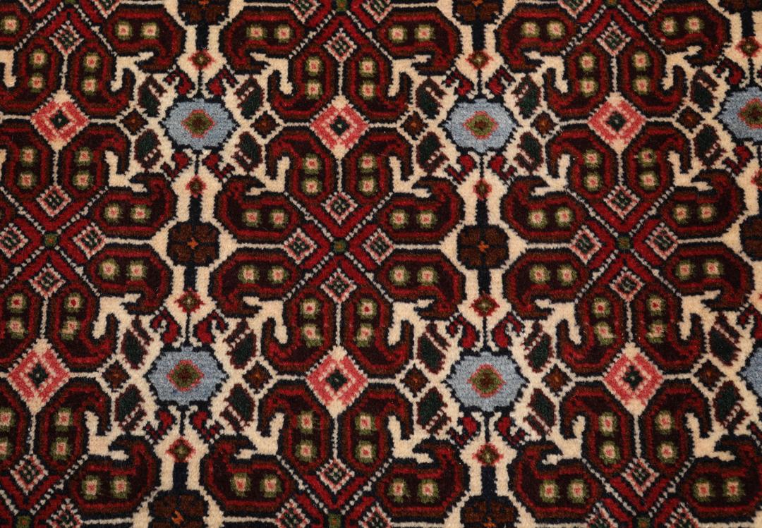 A hand-knotted Senneh rug from the Middle East featuring a dark-red field with geometric motifs.