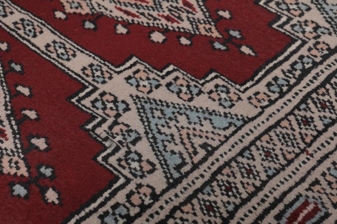 A rectangular hand-knotted Pakistan Bokhara rug with a deep red field and geometric motifs.