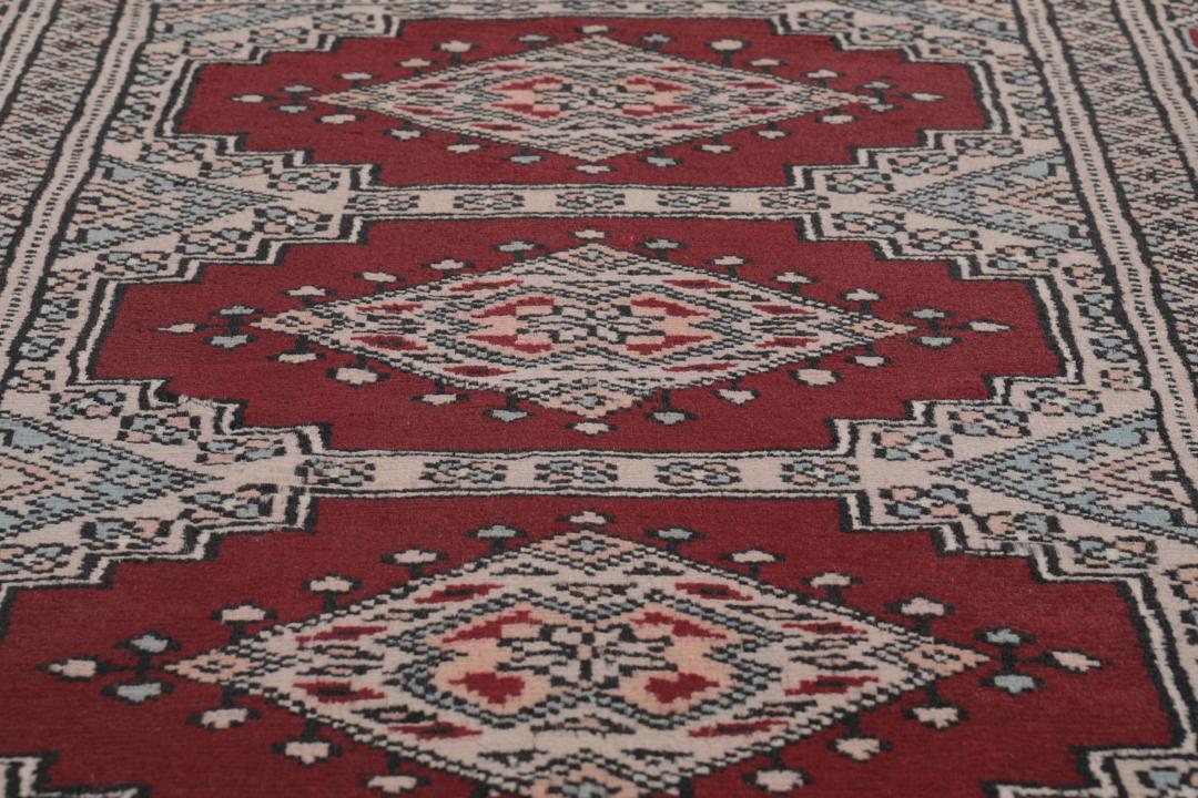 A rectangular hand-knotted Pakistan Bokhara rug with a deep red field and geometric motifs.