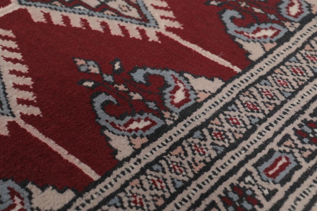 A rectangular hand-knotted Pakistan Bokhara rug with a deep red field and geometric motifs.