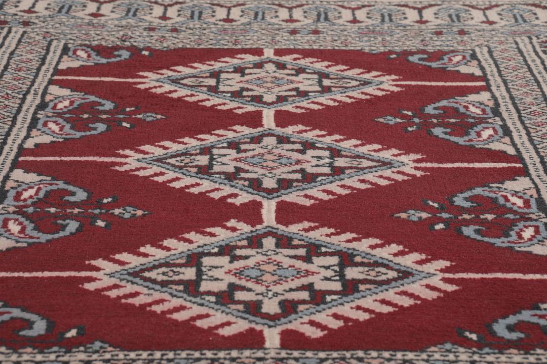 A rectangular hand-knotted Pakistan Bokhara rug with a deep red field and geometric motifs.
