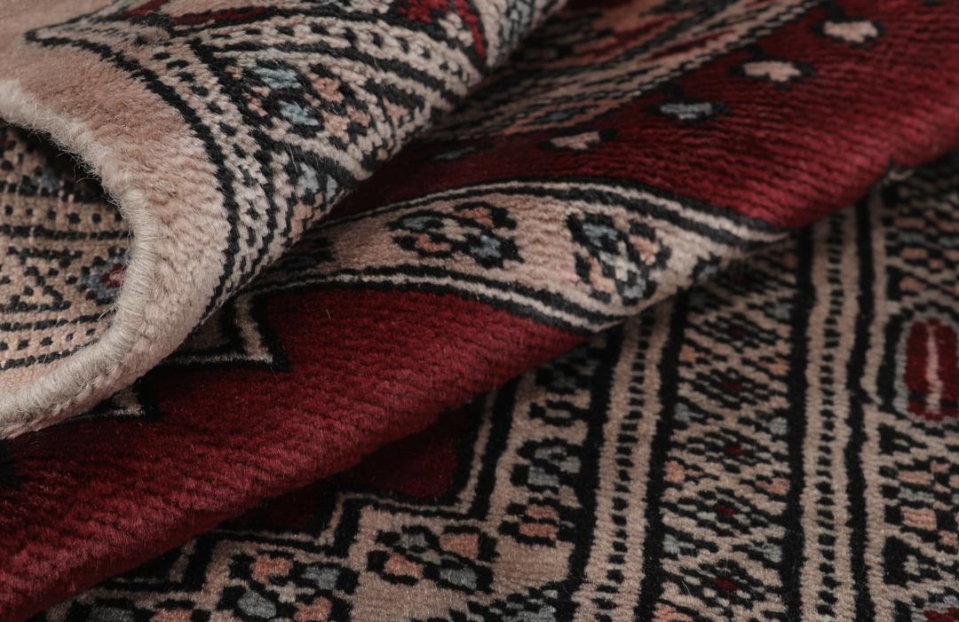 A rectangular hand-knotted Pakistan Bokhara rug with a deep red field and geometric motifs.