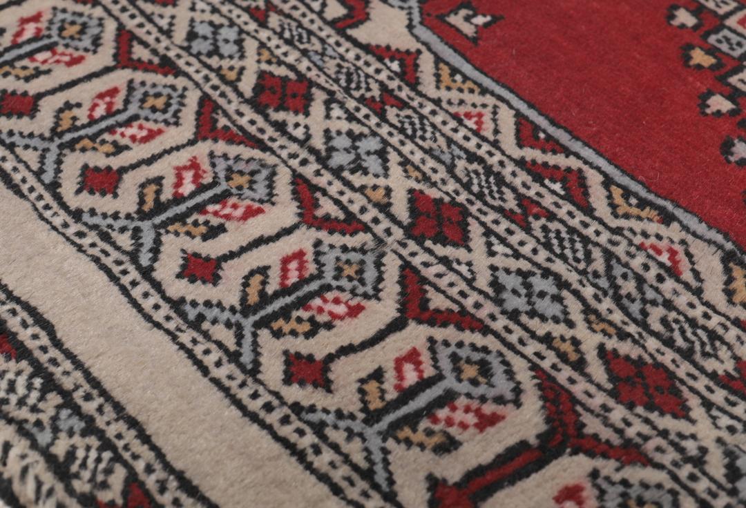 A red and beige hand-knotted Pakistan Bokhara rug with traditional geometric motifs.