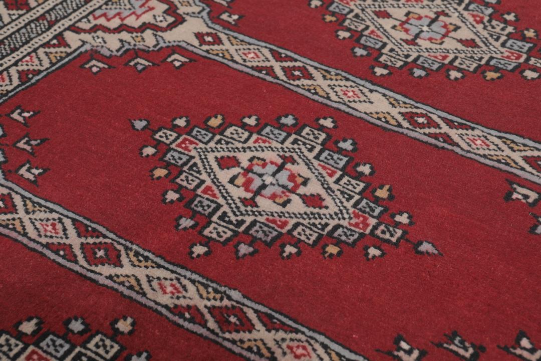 A red and beige hand-knotted Pakistan Bokhara rug with traditional geometric motifs.