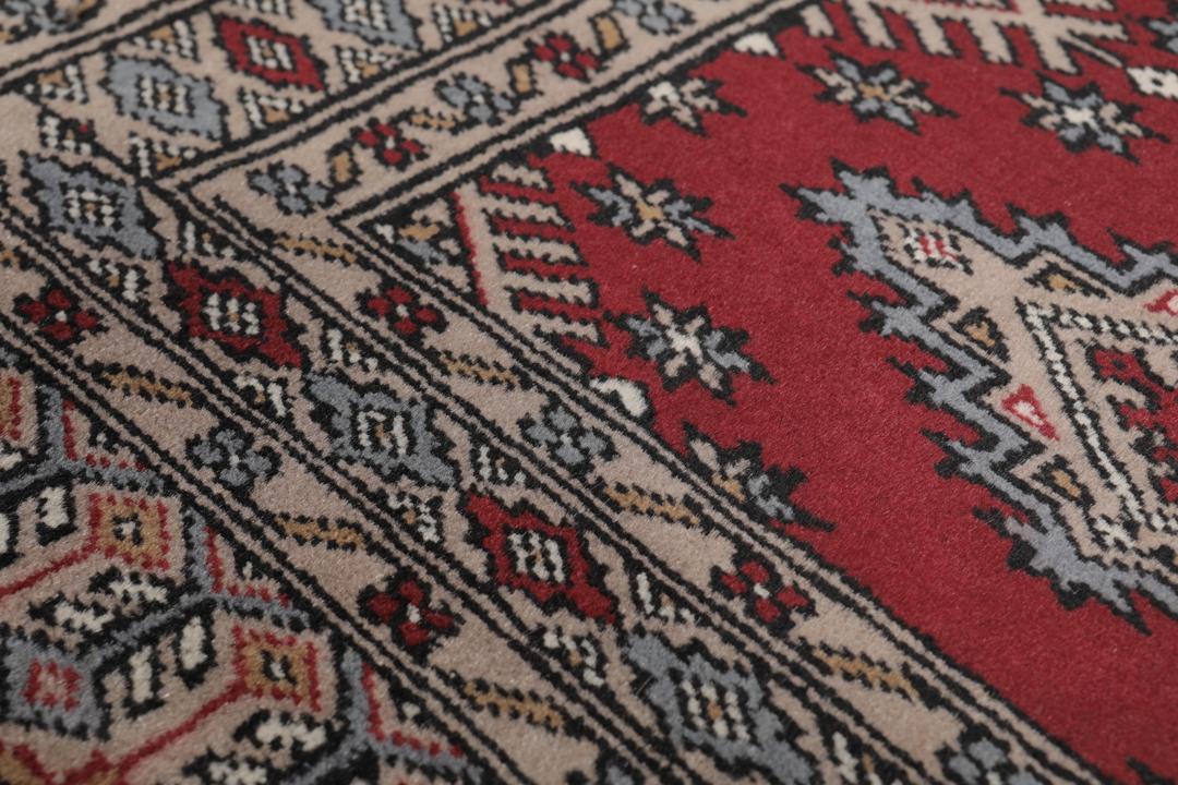 A red and beige hand-knotted Pakistan Bokhara rug with traditional geometric motifs.