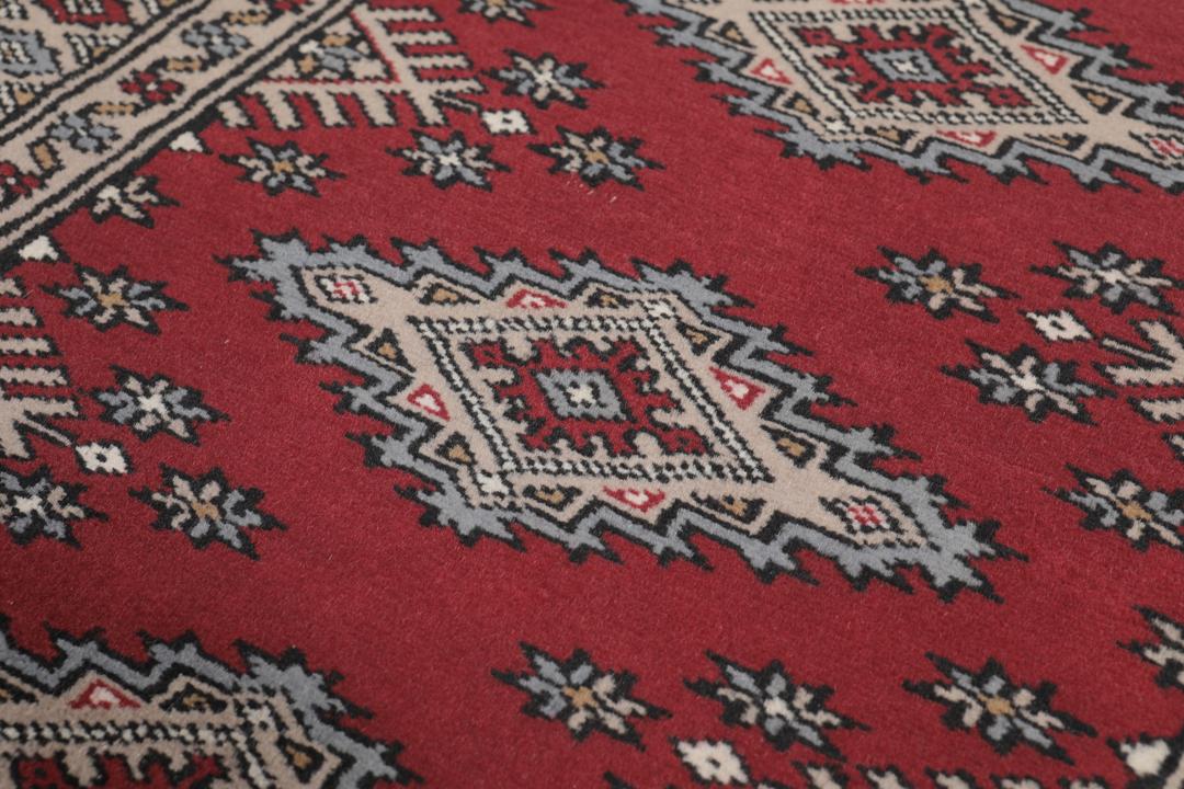 A red and beige hand-knotted Pakistan Bokhara rug with traditional geometric motifs.