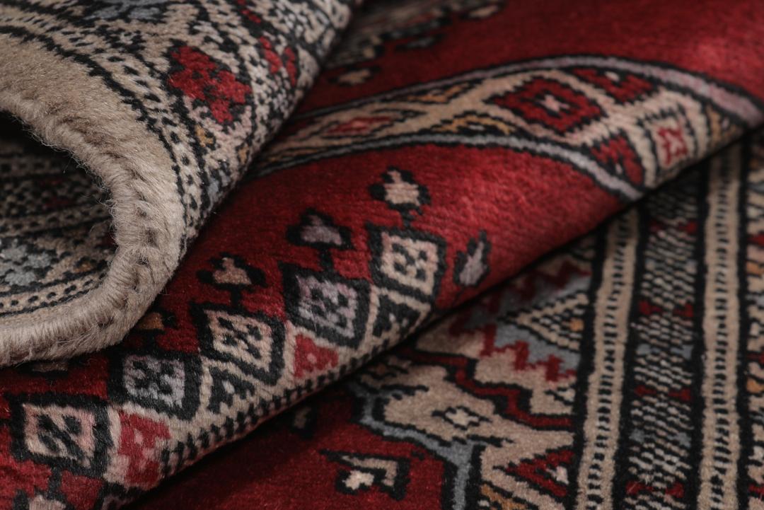 A red and beige hand-knotted Pakistan Bokhara rug with traditional geometric motifs.