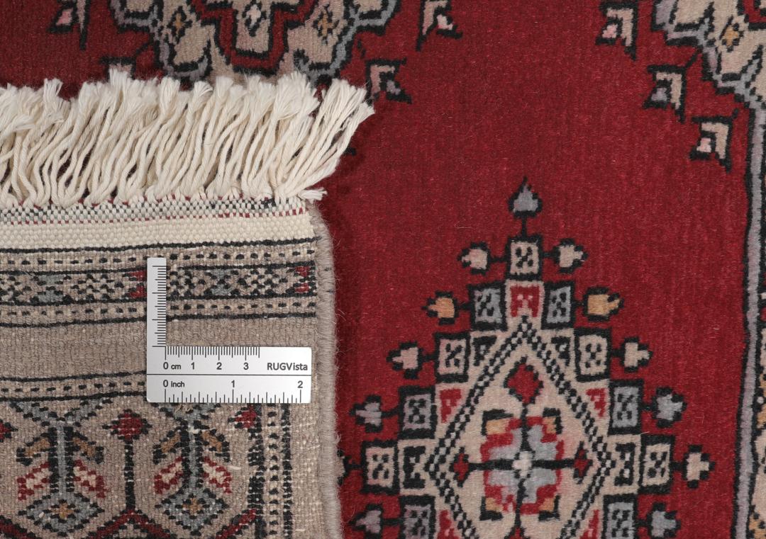A red and beige hand-knotted Pakistan Bokhara rug with traditional geometric motifs.