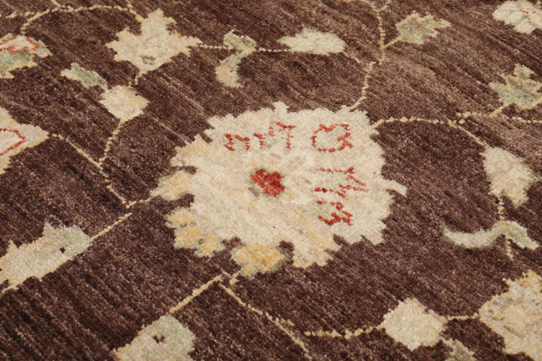 A hand-knotted Afghan rug with a dark brown field and ornate floral patterns.