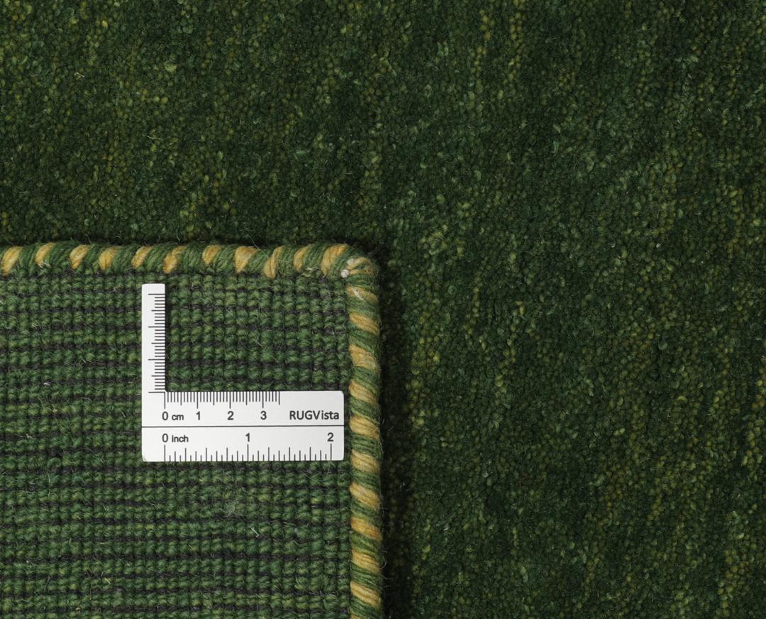 Een groen handgeknoopt wollen tapijt met minimale kleurrijke motieven.