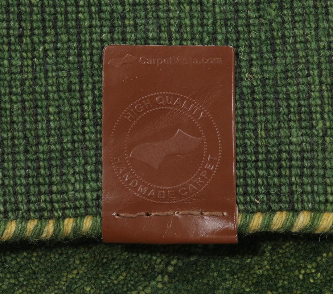 Een groen handgeknoopt wollen tapijt met minimale kleurrijke motieven.