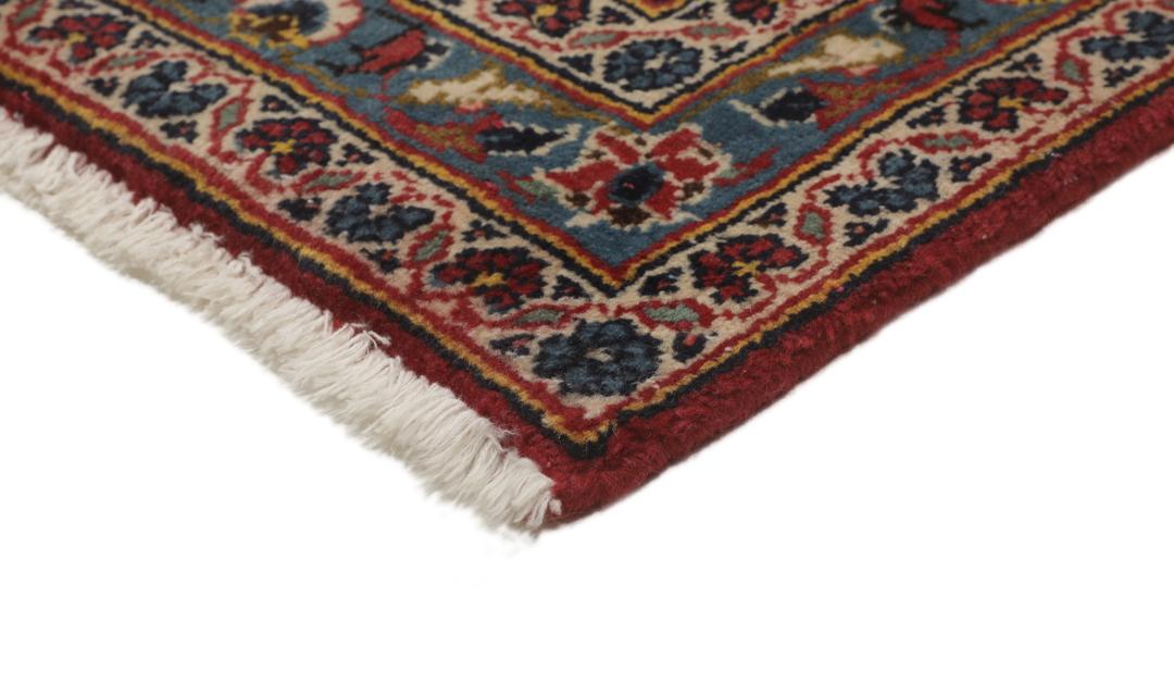 Een handgeknoopt Keshan-tapijt uit het Midden-Oosten met een rood veld en donkerblauwe randen.