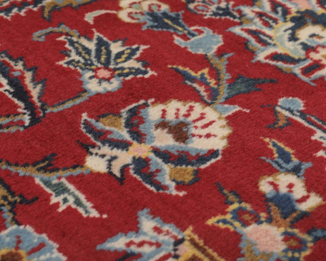 A hand-knotted Keshan rug from the Middle East with a red field and intricate floral patterns.