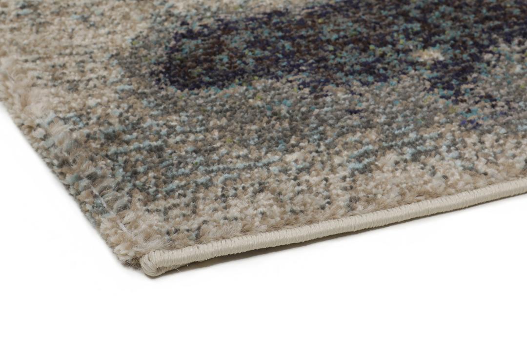 Et rektangulært tæppe med et abstrakt malerisk mønster i nuancer af creme, beige og grøn.