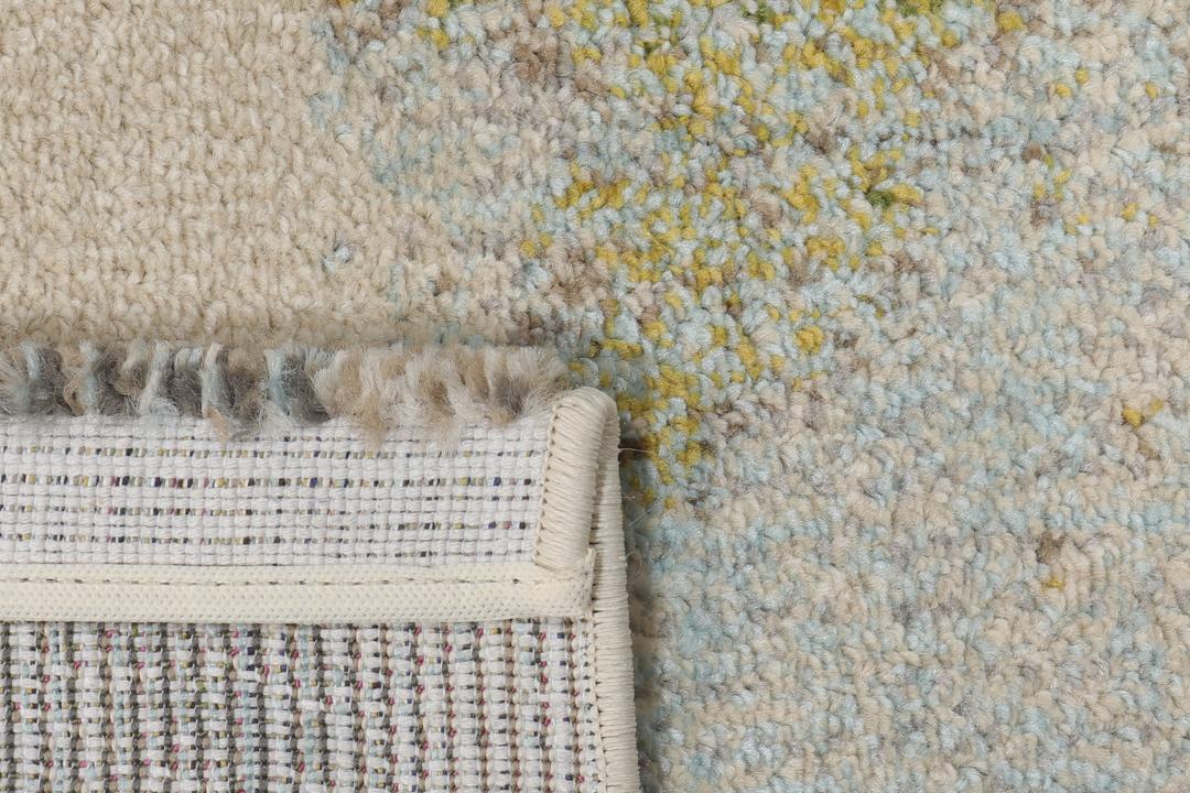 Et rektangulært tæppe med et abstrakt malerisk mønster i nuancer af creme, beige og grøn.