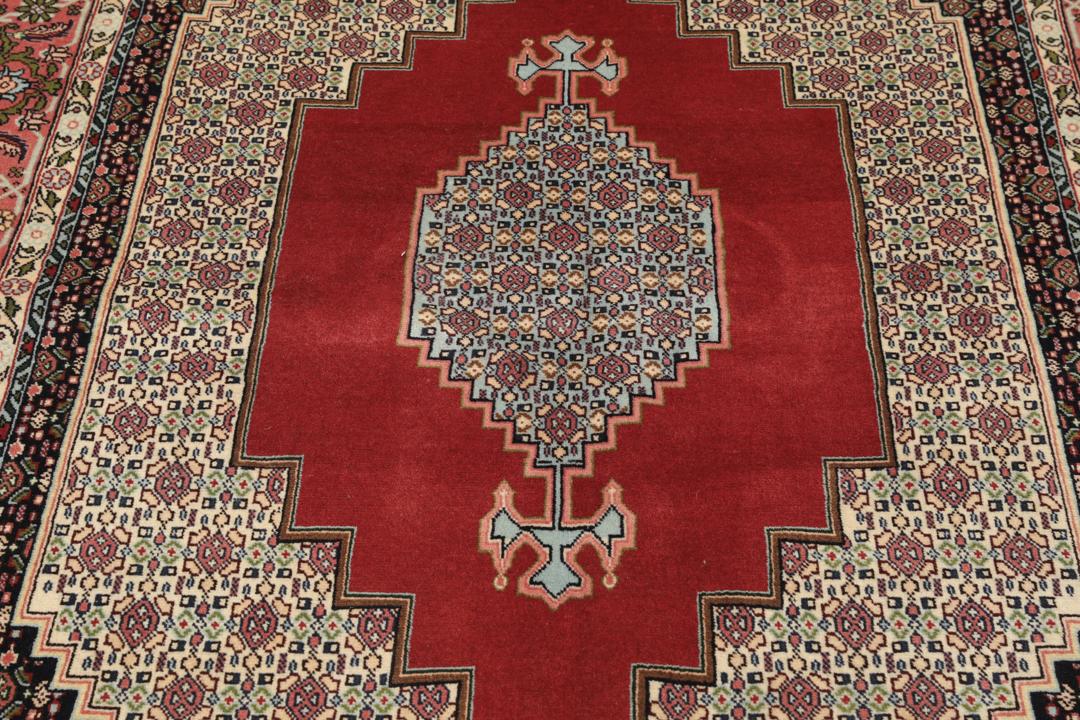 A hand-knotted Senneh rug from the Middle East featuring a dark-red and cream geometric medallion design.