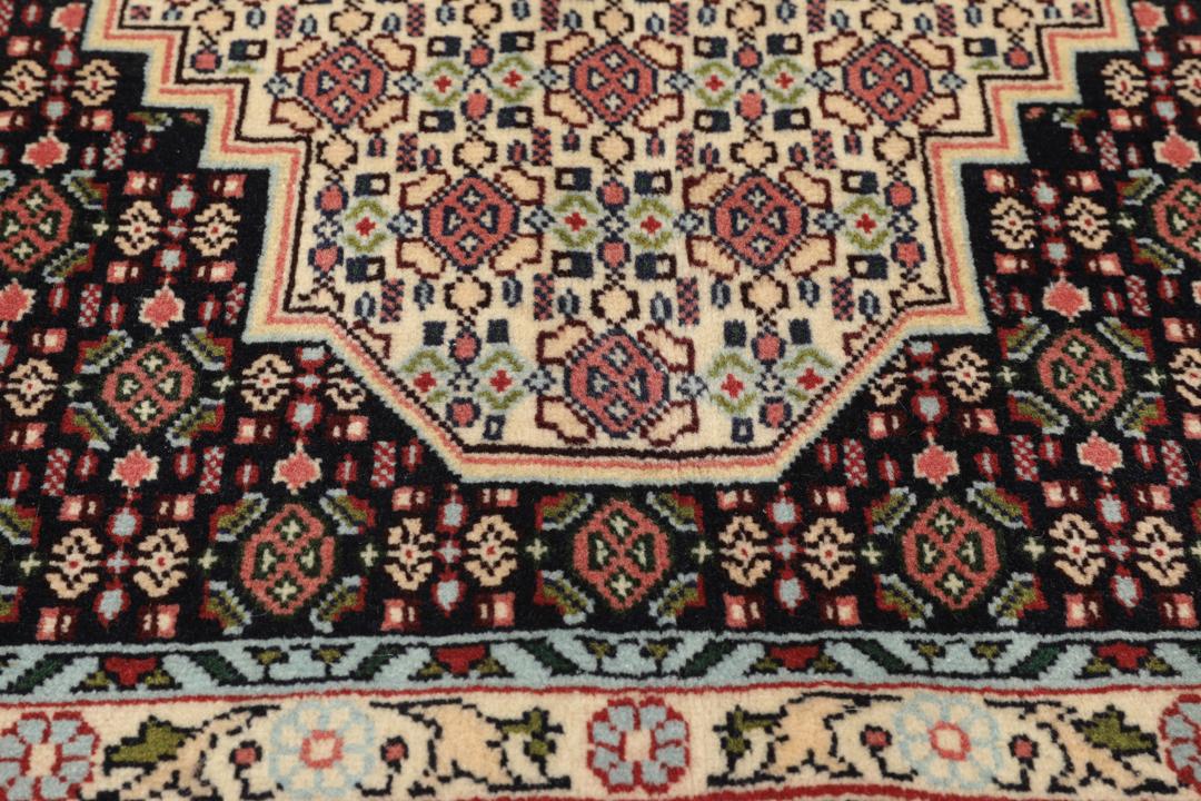 A hand-knotted Senneh rug from the Middle East featuring a dark-red and cream geometric medallion design.