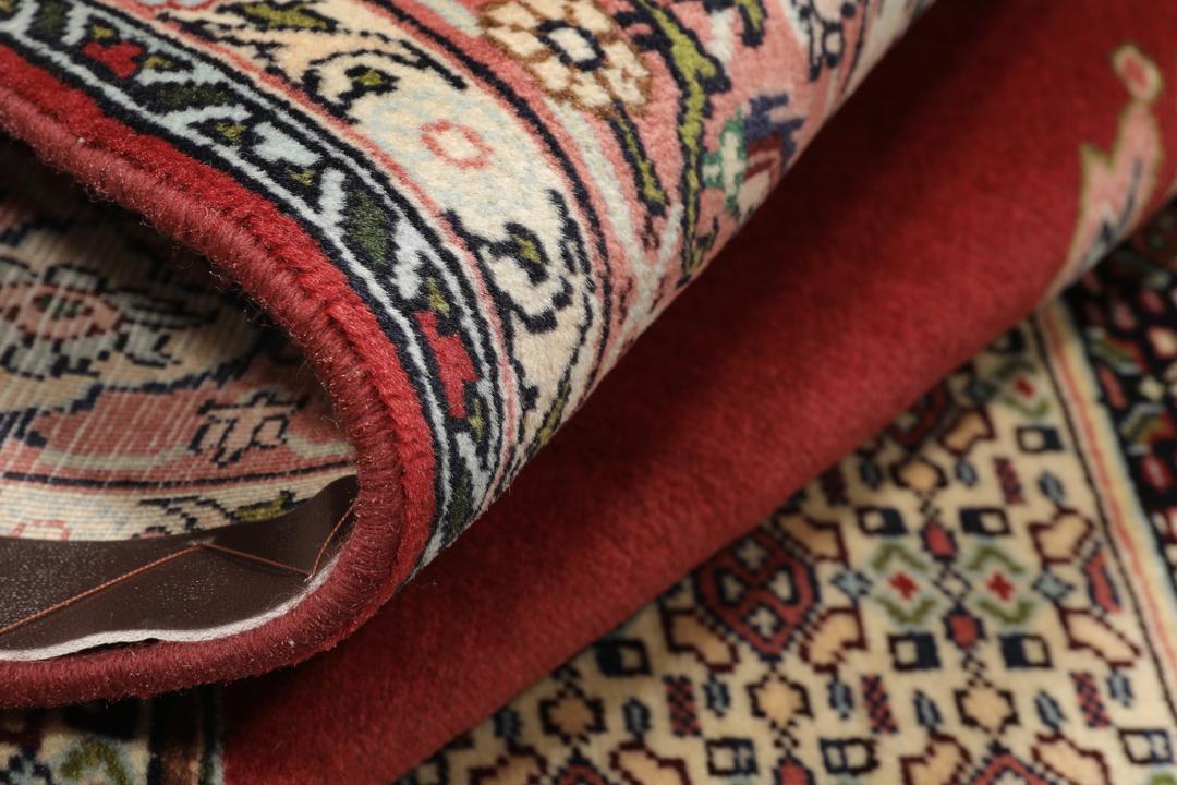 A hand-knotted Senneh rug from the Middle East featuring a dark-red and cream geometric medallion design.