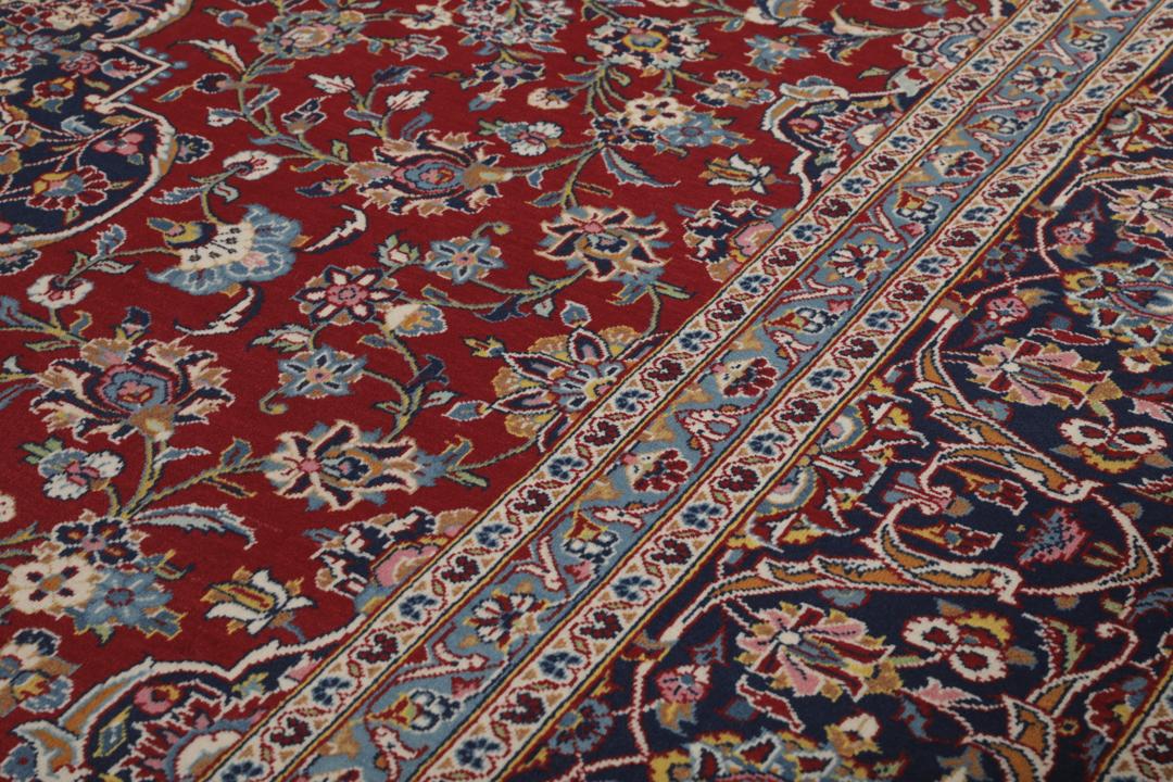 Una alfombra Keshan anudada a mano del Medio Oriente con un campo rojo y bordes azul marino.