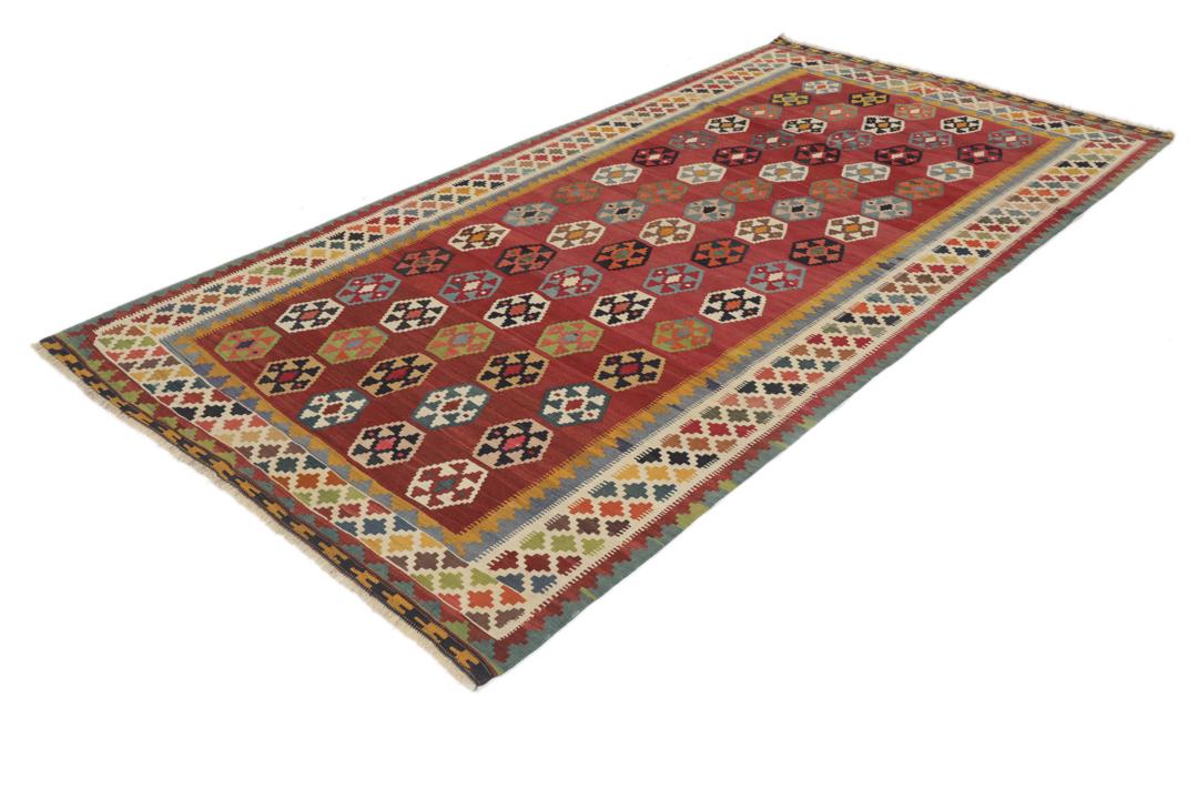 Een vintage handgeweven kelimkleed uit het Midden-Oosten met een rood veld en kleurrijke geometrische patronen.