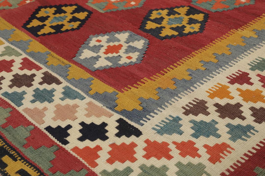 Een vintage handgeweven kelimkleed uit het Midden-Oosten met een rood veld en kleurrijke geometrische patronen.
