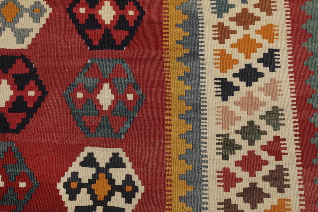 Een vintage handgeweven kelimkleed uit het Midden-Oosten met een rood veld en kleurrijke geometrische patronen.