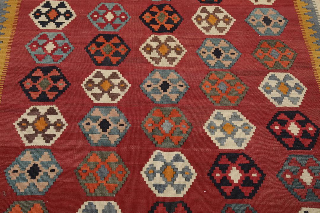 Een vintage handgeweven kelimkleed uit het Midden-Oosten met een rood veld en kleurrijke geometrische patronen.
