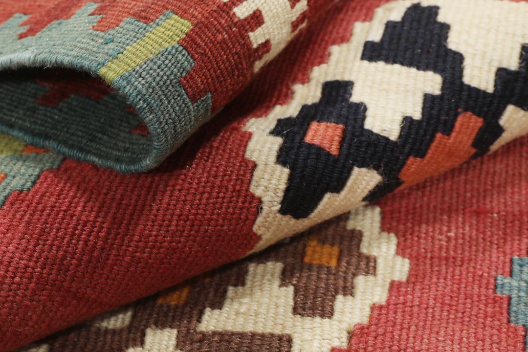 Een vintage handgeweven kelimkleed uit het Midden-Oosten met een rood veld en kleurrijke geometrische patronen.