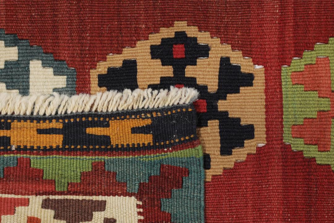 Een vintage handgeweven kelimkleed uit het Midden-Oosten met een rood veld en kleurrijke geometrische patronen.