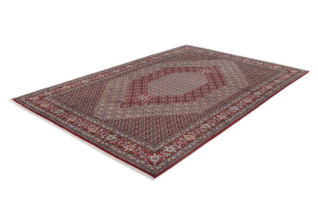Een handgeknoopt rood Senneh-tapijt met een centraal medaillonpatroon uit het Midden-Oosten.