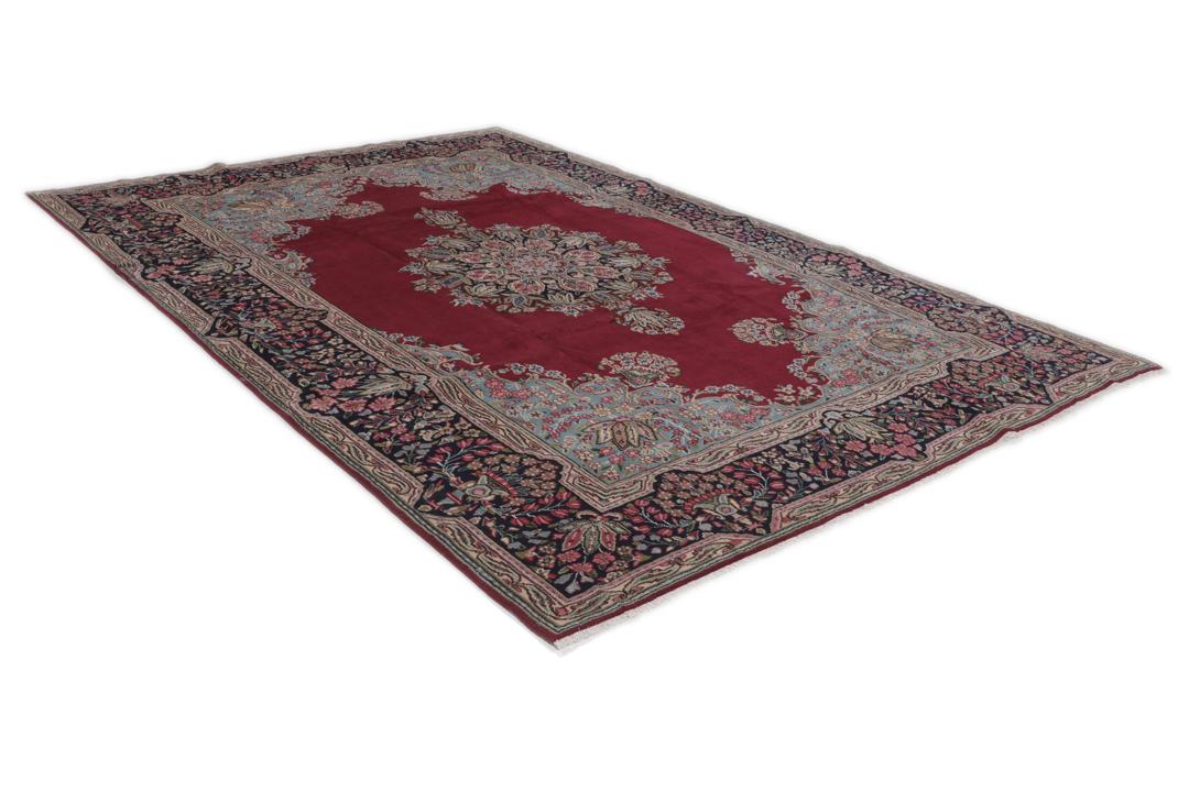 A hand-knotted Kerman rug with a red field and intricate floral medallion patterns.