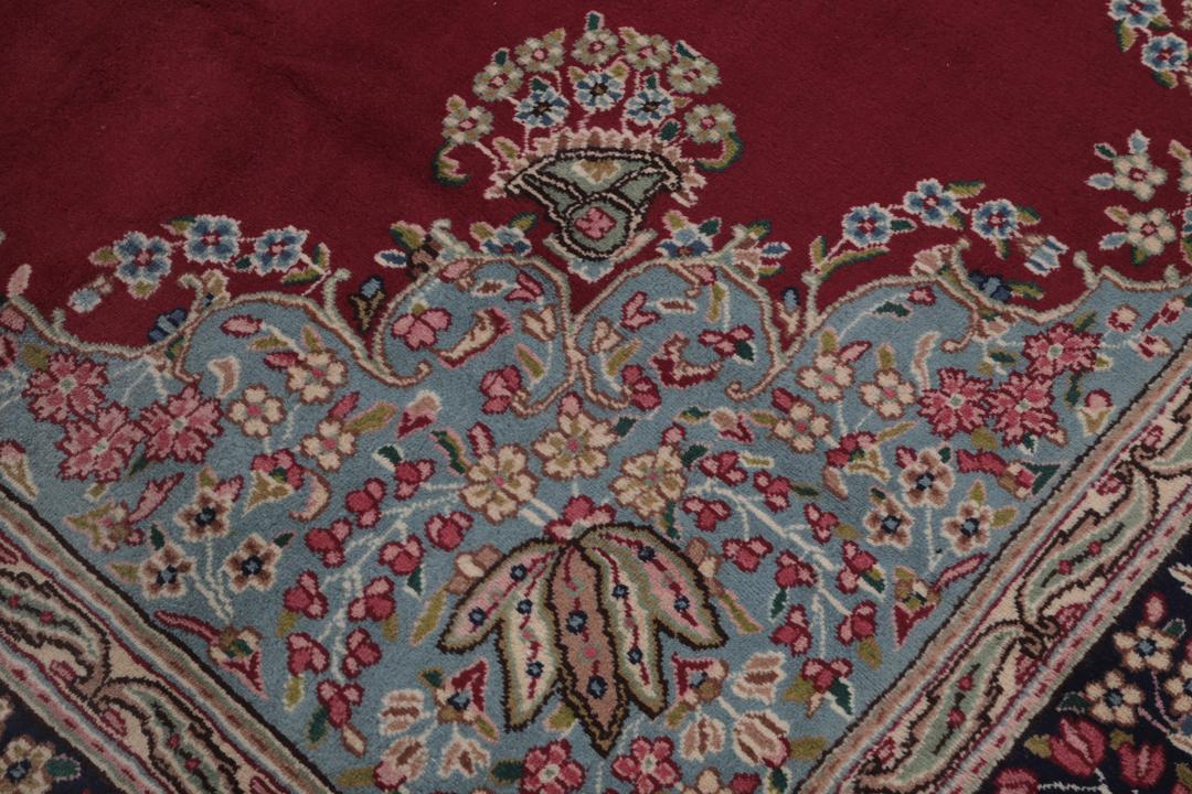 A hand-knotted Kerman rug with a red field and intricate floral medallion patterns.