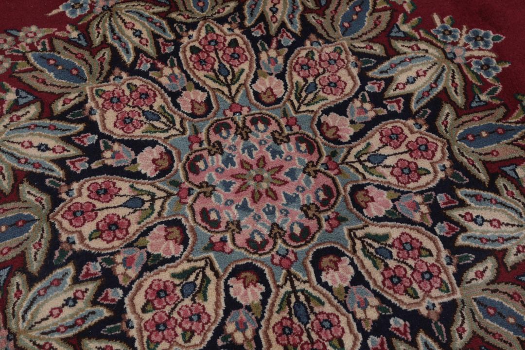 A hand-knotted Kerman rug with a red field and intricate floral medallion patterns.
