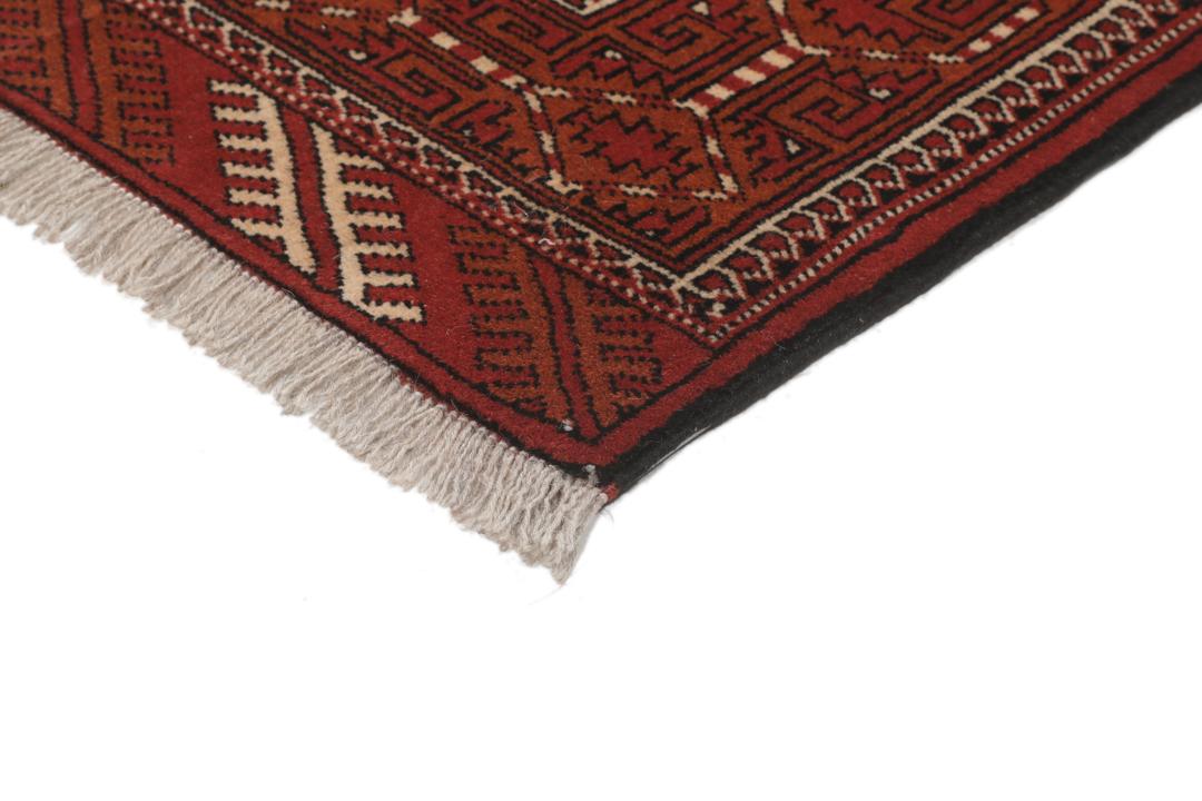 Een handgeknoopt Turkaman-tapijt met geometrische medaillons in rode en beige tinten.