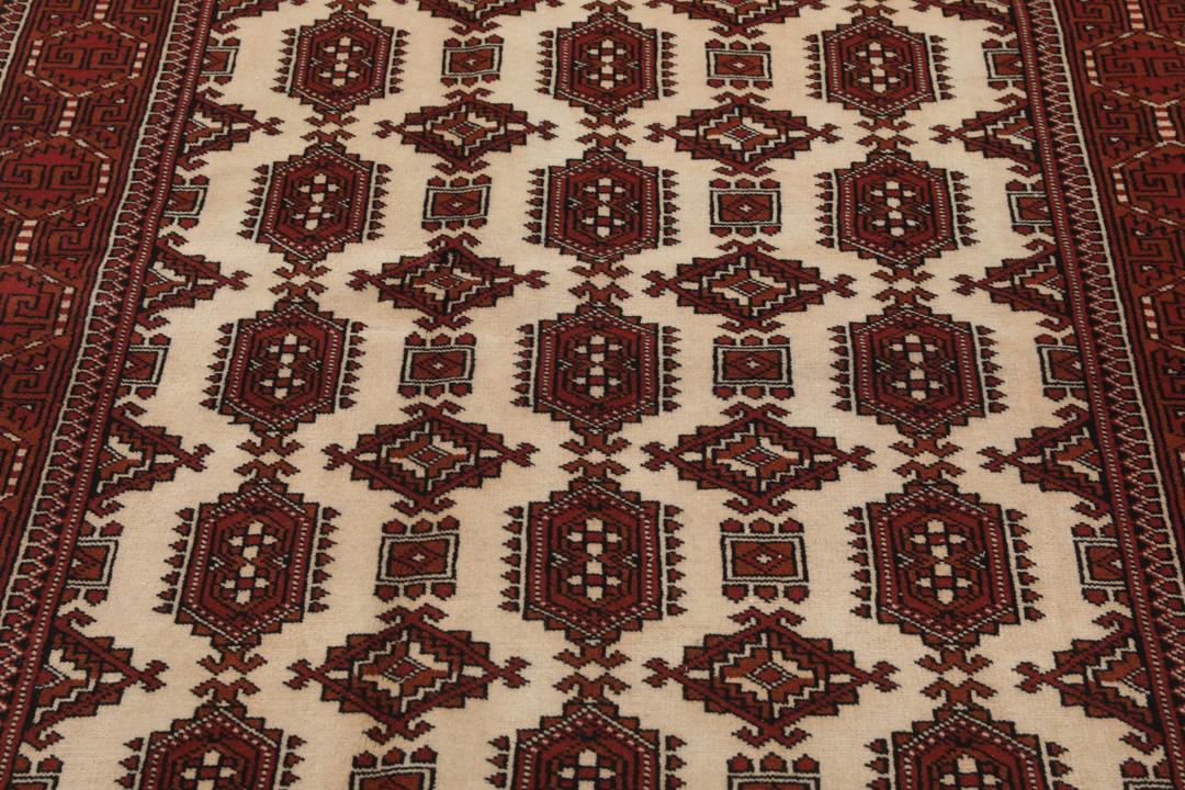 Een handgeknoopt Turkaman-tapijt met geometrische medaillons in rode en beige tinten.